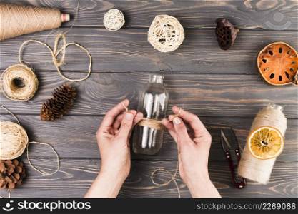 female hand tying glass bottle with string near cutter dry lotus pod dried fruit slices pine cone textured wooden surface