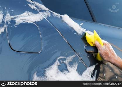 Female hand with a yellow sponge washes the car door handle