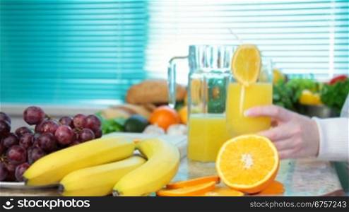 Female hand with glass of orange juice in the kitchen near a lot of vegetables and fruits
