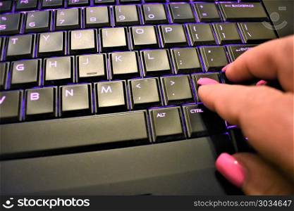 Female hand with manicure typing black and purple computer keyboard
