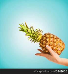 Female hand with pineapple at blue background, copy space for your design