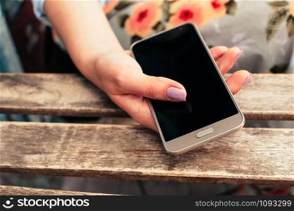Female hand with pink manicure holding smart phone with blank screen. Woman using electronic gadget at cafe