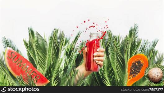 Female hand with red drink bottle: juice or smoothie leaned out of jungle with fruits , coconut and water melon with text summer at white background. Healthy lifestyle. Summer mood. Splash.