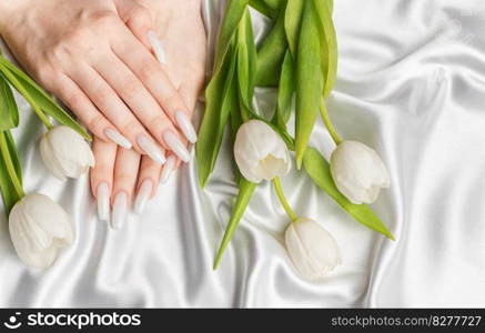 Female hand with spring nail design. White nail polish manicure. Female model hand with perfect manicure hold white tulip flowers on white silk background