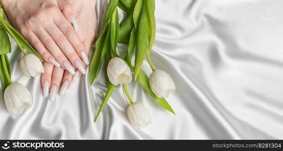 Female hand with spring nail design. White nail polish manicure. Female model hand with perfect manicure hold white tulip flowers on white silk background