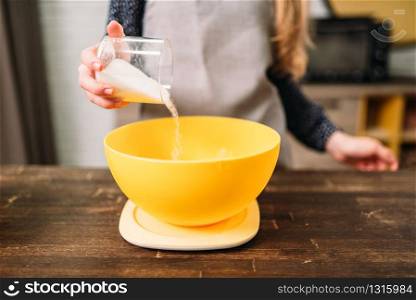 Female hands adds sugar into a bowl with dough on wooden table. Tasty cake cooking preparation