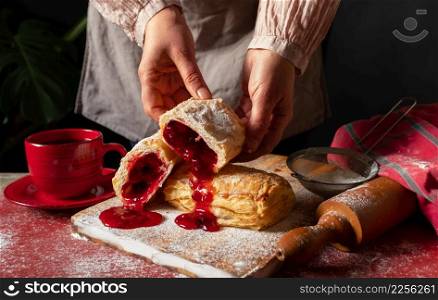 Female Hands bakes a Puff staffed with plum or red currant jam on the table.. Puff pastry dessert red jam hand viburnum cherry cup coffee black background