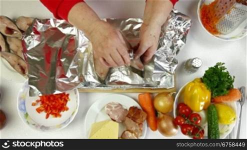 Female hands cooking baked fish - add salt and pepper Shoot from above