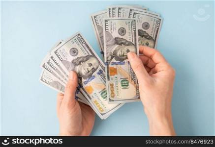 Female hands counting 100 dollar bills isolated on a blue background. Female hands counting 100 dollar bills isolated on a blue background.