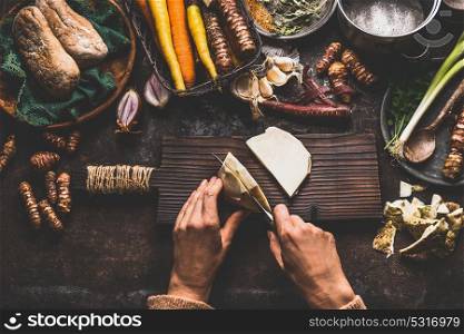 Female hands cutting celery on dark rustic kitchen table background with various vegetables and utensils. Root vegetables cooking preparation for tasty autumn dishes, top view. Healthy eating concept