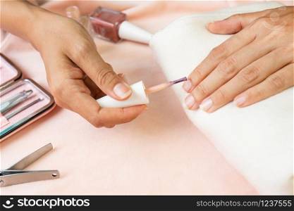 Female hands doing nail polish in pearl pink color with set of manicure instruments and tools on pink silk velvet. beauty, manicure concept