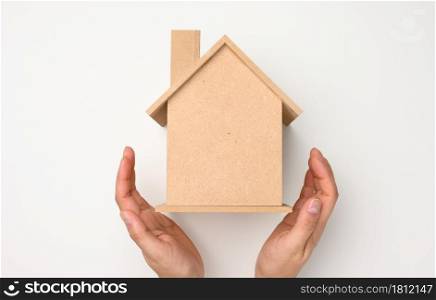 female hands folded to each other over a wooden miniature model house on a white background. Real estate insurance concept, environmental protection, family happiness