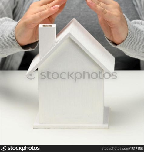 female hands folded to each other over a wooden miniature model house on a white background. Real estate insurance concept, environmental protection, family happiness