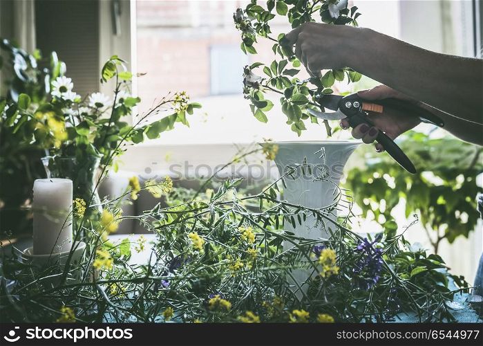 Female hands Hands cut flowers for summer bouquet with wild flowers on a table in modern living room at window. Summer still life. Cozy home scene