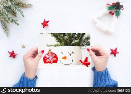 female hands hold a greeting Christmas card on the background of a white table with Christmas decor.
