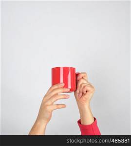 female hands hold a red ceramic mug, gray background