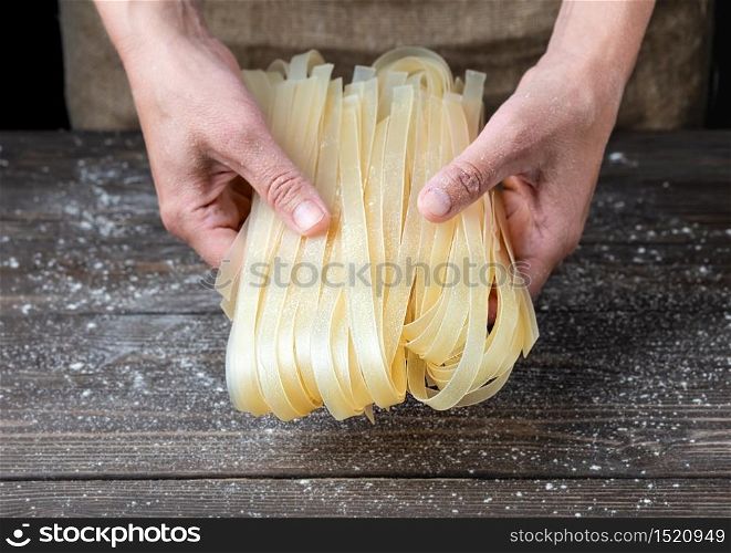 Female hands hold cooked noodles. Cooking noodles at home, close-up, dark wooden background, flour scattered on the table.. Female hands hold cooked noodles.