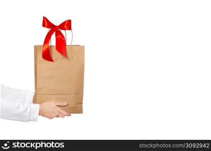 Female hands hold large gift bag made of brown craft paper with a red bow isolated on white background. Gift, present or e-shopping concept. Banner with copy space.. Female hands hold large gift bag made of brown craft paper with a red bow isolated on white background. Gift, present or e-shopping concept. Banner with copy space
