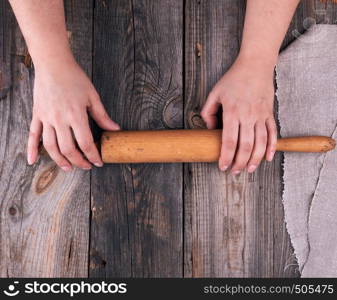 female hands hold old wooden rolling pin on a wooden table, top view