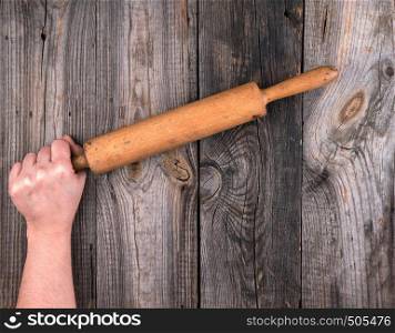 female hands hold old wooden rolling pin on a wooden table, top view