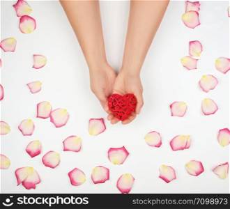 female hands hold red heart, white background with pink rose petals, top view, holiday backdrop