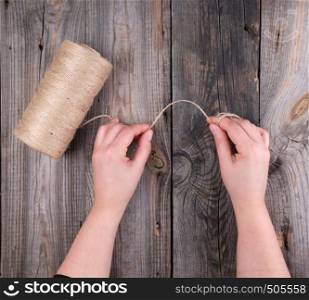 female hands holding a brown rope on a gray wooden table, top view