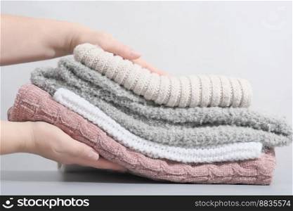 female hands holding a pile pastel color jumpers and other knitted clothing. winter apparel, trendy pale textured knitwear. cozy fall pullovers. female hands holding a pile pastel color jumpers and other knitted clothing. winter apparel, trendy pale textured knitwear. cozy fall pullovers. 