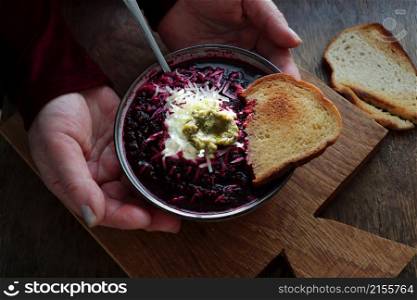 Female hands holding a plate vegetable soup with beetroot, cheese , sour cream and bread on arustic wooden background .. Female hands holding a plate vegetable soup with beetroot, cheese , sour cream and bread on arustic wooden background