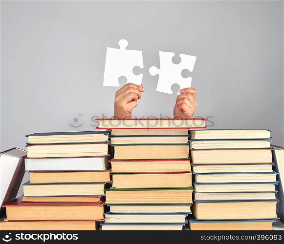 female hands holding big white puzzles over a stack of books, gray background