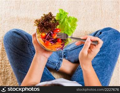 Female hands holding bowl with green lettuce salad on legs, Above young woman eating fresh salad meal vegetarian spinach in a bowl, Clean detox healthy homemade food concept