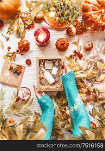 Female hands holding box with cosmetic products on desktop with autumn leaves, pumpkins,burning candles and cup of hot chocolate or coffee. Skincare routine for fall. Beauty box. Flat lay. Blog layout