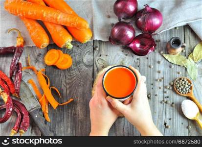 Female hands holding carrot juice in an iron mug, top view