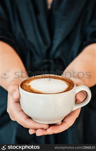 Female hands holding cup of beautiful hot Coffee Capuccino with nice milk form on top, close up shot