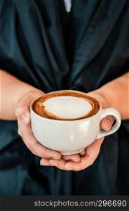 Female hands holding cup of beautiful hot Coffee Capuccino with nice milk form on top, close up shot