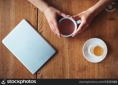 Female hands holding cup top view on wooden background.