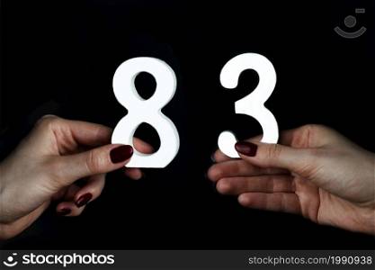 Female hands holding figures eighty-three on a black background.. Female hands holding numbers eighty-three.