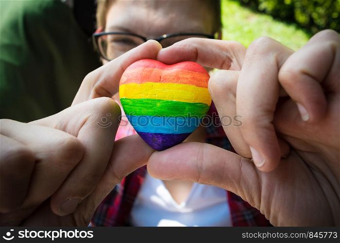 Female hands holding heart with rainbow stripes. LGBT pride flag, symbol of lesbian, gay, bisexual, transgender for social movements. Homosexual love, Human rights concept. Copy space.. Female hands holding decorative Heart with rainbow stripes. LGBT pride flag, symbol of lesbian, gay, bisexual, transgender for social movements. Homosexual love, Human rights concept. Copy space.