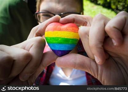 Female hands holding heart with rainbow stripes. LGBT pride flag, symbol of lesbian, gay, bisexual, transgender for social movements. Homosexual love, Human rights concept. Copy space.. Female hands holding decorative Heart with rainbow stripes. LGBT pride flag, symbol of lesbian, gay, bisexual, transgender for social movements. Homosexual love, Human rights concept. Copy space.