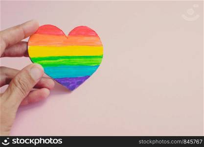 Female hands holding heart with rainbow stripes on pink background. LGBT pride flag, symbol of lesbian, gay, bisexual, transgender, social movements. Homosexual love, Human rights concept. Copy space.. Female hand holding decorative Heart with rainbow stripes on pink background. LGBT pride flag, symbol of lesbian, gay, bisexual, transgender. Homosexual love, Human rights concept. Copy space.