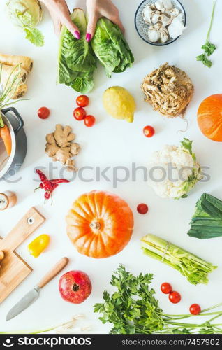 Female hands holding lettuce on white table background  with pumpkins and various seasonal vegetables, pot ,cutting board and knife. Harvest cooking. Flat lay. Healthy lifestyle and eating. Low carb