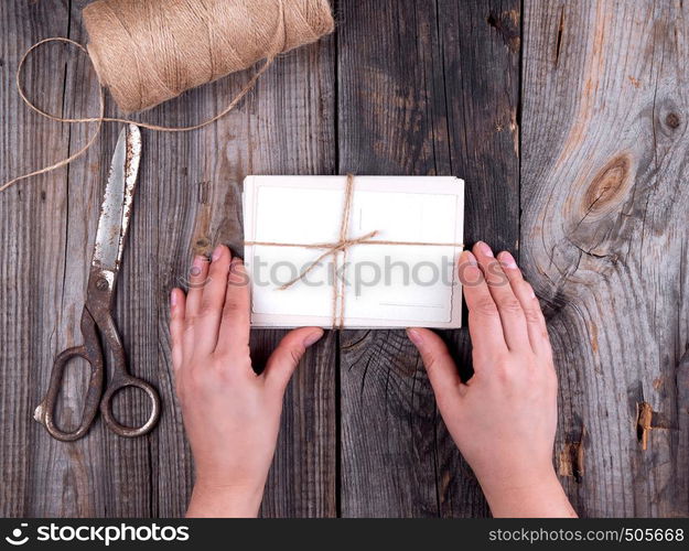 female hands holding old paper postcards tied with rope on gray wooden background, top view