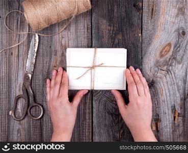 female hands holding old paper postcards tied with rope on gray wooden background, top view