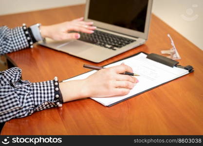 Female hands holding pen under the document and working with laptop at the table in an office. Female working with the documents