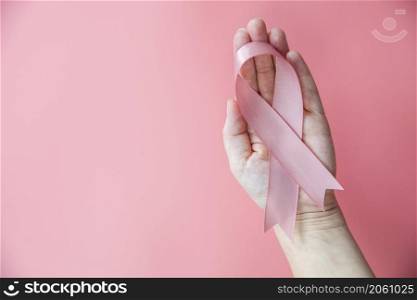 Female hands holding pink ribbon over pink background, breast cancer awareness, October pink concept top view with copy space, health, woman cancer concept space for text. Female hands holding pink ribbon over pink background, breast cancer awareness, October pink concept top view with copy space, health, woman cancer concept