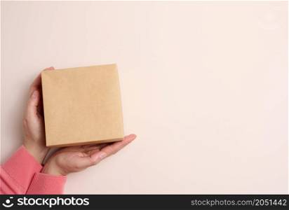 female hands holding square cardboard gift box on beige background, top view