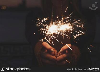 Female hands holding two burning sparklers in front of middle part of the body. Female hands holding two burning sparklers