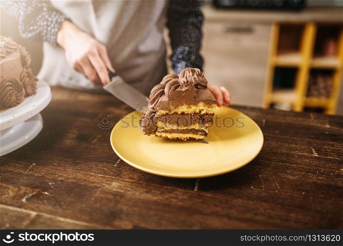 Female hands holds piece of chocolate cake on the blade, culinary masterpiece. Kitchen on background. Homemade sweet dessert