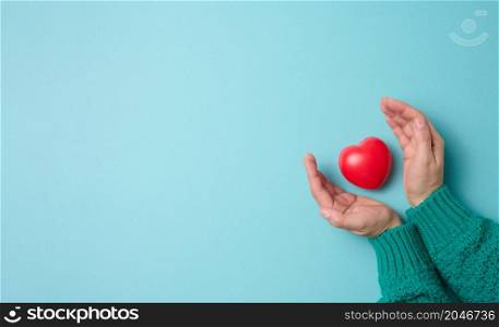 female hands holds red heart, blue background. Love and donation concept, copy space, top view