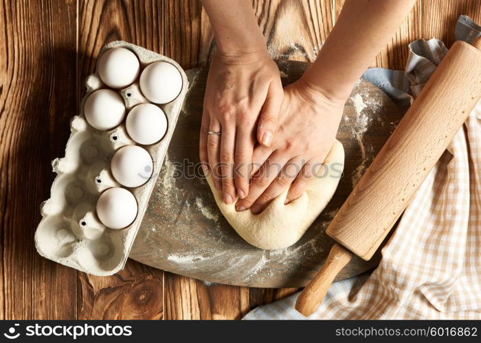 Female hands kneading dough on wooden table