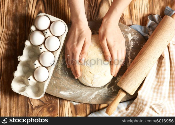 Female hands kneading dough on wooden table